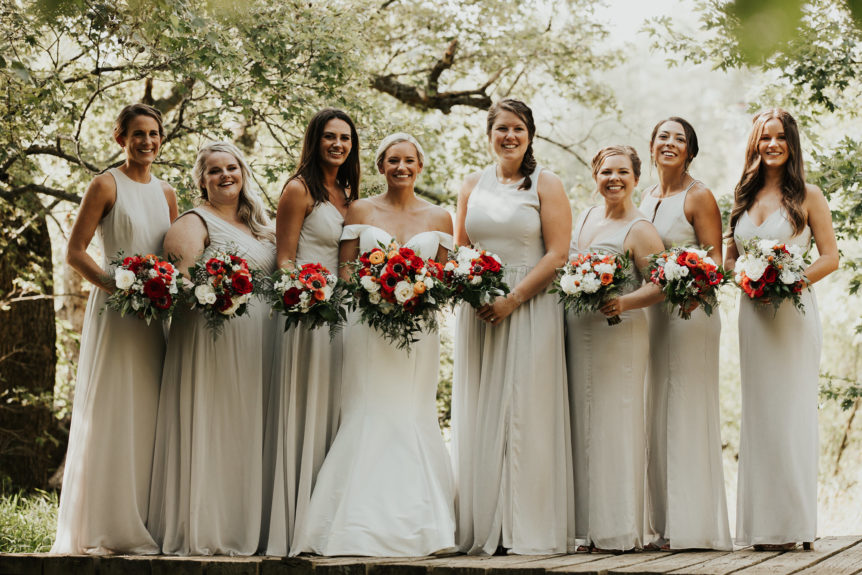 Bride and bridesmaids in soft cream dresses holding colorful bouquets.