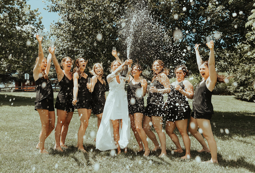 Bride and bridesmaids sharing a fun moment with a champagne bubble splash photo op at Zion Springs, a barn wedding venue in Northern Virginia.