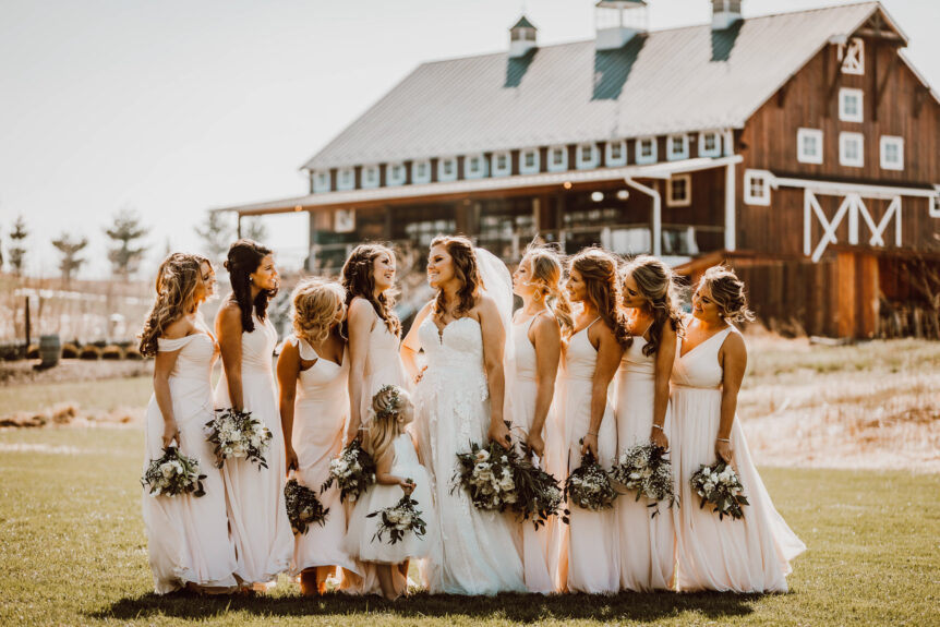 Brides and bridesmaids sharing a fun moment by the barn at Zion Springs, a rustic elegant wedding venue in Virginia.